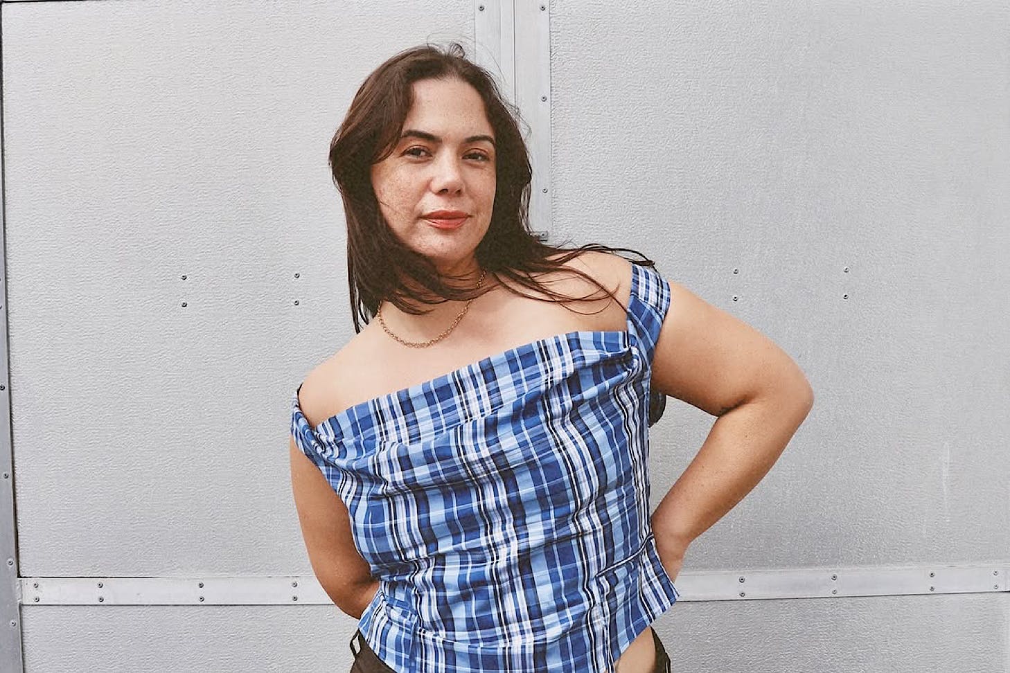 A woman wears an off-the-shoulder blue and black chequered top by Riel, one of NZ's best sustainable fashion labels.